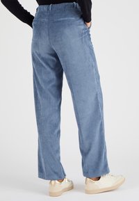 Pantalons en velours côtelé bleu clair avec une coupe décontractée, dotés de poches latérales et d'une taille élastique, associés à des baskets blanches avec des accents dorés.
