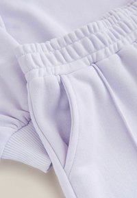 Lyse lilla sportstøj med elastisk talje, struktureret stof og sidelommer. Glat, blød tekstur med ribbede detaljer.