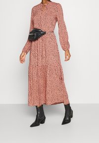 Dlouhé růžové šaty s černým puntíkovaným vzorem, s plisovanou sukní a nafouklými rukávy. Stylizované s černou ledvinkou a kotníkovými botami.