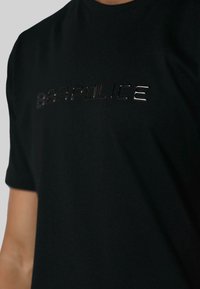 Juodas medvilninis marškinėlis su blizgiu, iškilniu "POLICE" logotipu ant krūtinės. Trumpomis rankovėmis ir apvaliu iškirpimu.