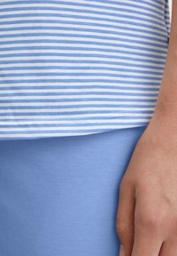 Blauw-wit gestreepte top met een zachte textuur, gecombineerd met een effen lichtblauwe onderkant. Close-up van de stof en handdetail.
