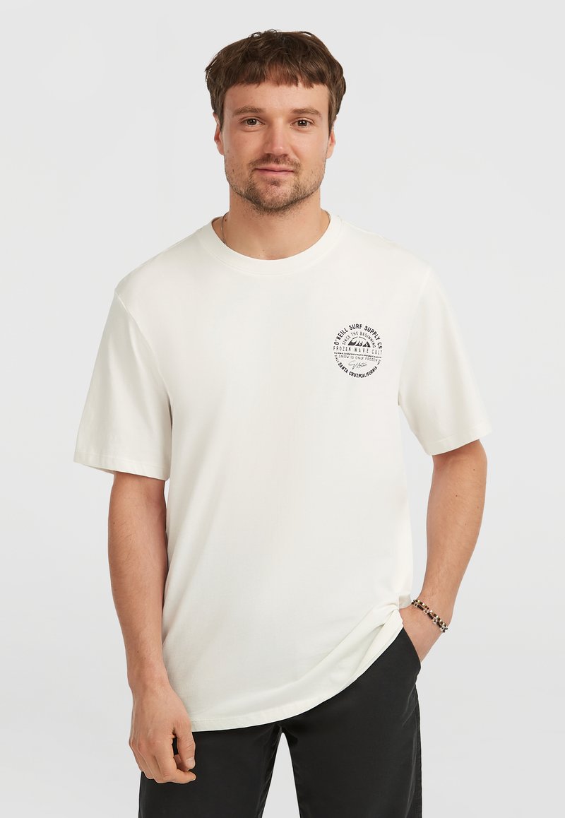 T-shirt bianca in cotone con scollatura rotonda e maniche corte. Presenta una stampa grafica circolare sul lato sinistro del petto. Indossata con pantaloni scuri.