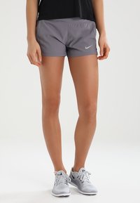 Grå atletiska shorts med elastisk midja och Nike swoosh-logotyp, tillsammans med ljusgrå löpskor. Lätt och smidigt material.