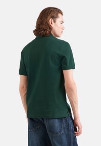 Ciemnozielona koszulka polo z krótkimi rękawami, wykonana z bawełnianego materiału, z klasycznym kołnierzykiem i bocznymi rozcięciami na końcu, w połączeniu z szortami dżinsowymi.