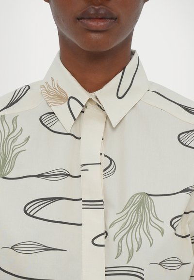 Camicia con colletto in tessuto crema caratterizzata da motivi astratti di foglie nere e verdi. Texture liscia con chiusura a bottone frontale.