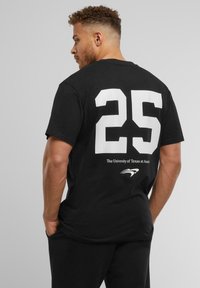 Sort bomulds T-shirt med et stort hvidt "25" på ryggen, med "The University of Texas at Austin" nedenunder og et logo accent.