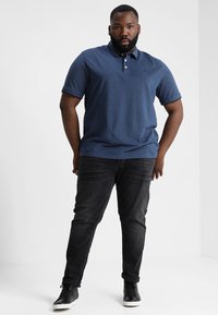Mørkeblå polo skjorte med krave og tre-knaps lukning, parret med mørke jeans og sorte højtop sneakers. Glat stofstruktur.
