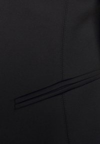 Tissu noir à la texture lisse, présentant un design de poche fine délimité par une couture contrastante. Éléments de design simples et fonctionnels présents.