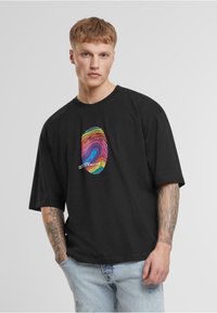 Fekete, oversize póló, amelynek közepén egy színes ujjlenyomat grafika található. Pamutból készült, rövid ujjú és laza szabású.