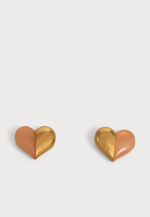 Paire de boucles d’oreilles en forme de cœur, moitié or brillant avec le motif GUESS gravé, moitié lisse marron clair, présentées sur un fond blanc.