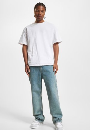 Weißes Baumwoll-T-Shirt mit kurzen Ärmeln, kombiniert mit hellblauen, lässigen Jeans und weißen Sneakers. Einfaches Design und lockere Passform.