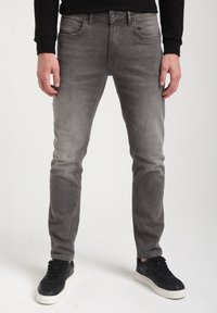 Harmaat farkut, joissa on slim fit -leikkaus, viisi taskua, hienovarainen kulunut pinta, ja ne on yhdistetty mustiin tennareihin.