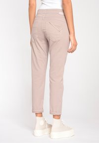 Ljusbruna tapered byxor med hög midja, uppvikta fållar och två bakfickor med vinklade lock. Bärs tillsammans med crèmefärgade högklackade sneakers.