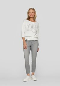 White knit sweater with a textured pattern and silver lettering, paired with light gray slim-fit pants and white sneakers.