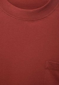 Maroon t-shirt made of cotton, featuring a round neckline, short sleeves, and a small pocket on the left side with a smooth texture.