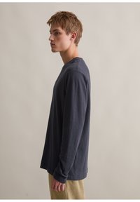 Langärmliges, marineblaues Baumwollhemd mit rundem Ausschnitt und lockerer Passform, kombiniert mit hellen, strukturierten Hosen.