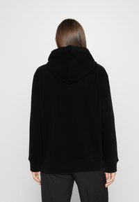 Sudadera negra con capucha fabricada con tela suave, con un ajuste holgado, mangas largas y sin patrones ni logotipos visibles.