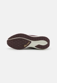 Suola della scarpa Nike, caratterizzata da una suola in gomma marrone textured con un' intersuola bianca e il marchio "Nike Storm+ Tread" in oro.