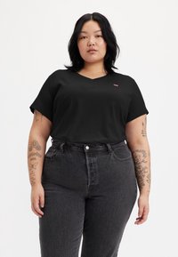 Black V-neck t-shirt, short sleeves, made of soft fabric. Worn with high-waisted black denim jeans, featuring visible stitching and pockets.