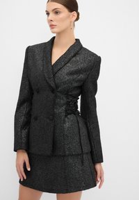 Blazer doppiopetto nero con texture, design aderente, dettaglio con lacci in vita e gonna coordinata.