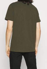 Olivově zelené tričko s krátkým rukávem, vyrobené z měkké látky, s volným střihem a kulatým výstřihem, s jednoduchým designem a bez viditelných vzorů.