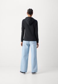 Felpa nera con vestibilità morbida e cappuccio con coulisse, abbinata a jeans a gamba larga blu chiaro e sneaker nere.