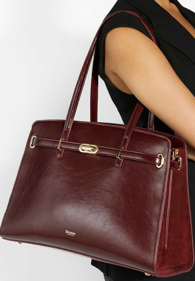 Burgundy leather handbag with a structured shape, dual handles, gold hardware accents, and a smooth texture. Brand logo visible on the front.
