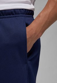 Marineblå sweatpants med elastisk talje og sidelomme. Stoffet har en blød tekstur og et sømløst design.