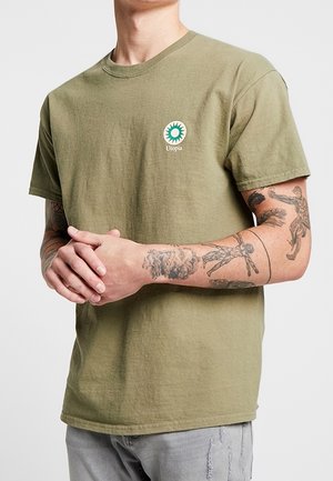 Camiseta de algodón verde oliva con cuello redondo, mangas cortas y un logotipo circular que presenta un estallido solar verde y el texto "Utopía".