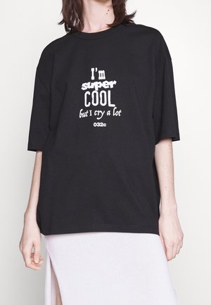 Osoba nosząca czarną, oversize'ową koszulkę z białym nadrukiem ""I'm super cool but I cry a lot 032c"" oraz białą spódnicę z bocznym rozcięciem.