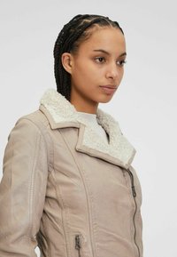 Beige leren jas met een witte nepbontkraag, zijrits, aansluitend ontwerp en een gestructureerd oppervlak.