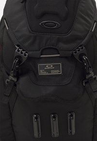 Black backpack featuring textured fabric, durable plastic hardware, adjustable straps, and a branded label with silver accents.