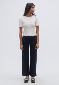 Ανοιχτό γκρι, υφασμάτινη κοντομάνικη μπλούζα συνδυασμένη με ψηλόμεσα, σκούρα μπλε φαρδιά τζιν παντελόνια και καφέ παπούτσια με διακοσμητικές λεπτομέρειες.