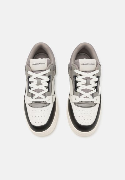 Witte en grijze sneakers met een leren en mesh bovenwerk, ronde neus, geperforeerde details en contrasterende zwarte accenten op de zool en zijkanten.