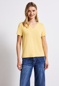 Geel V-hals T-shirt met korte mouwen, gemaakt van gladde stof, gecombineerd met blauwe denim wijde jeans. Eenvoudig ontwerp, zonder zichtbare patronen.