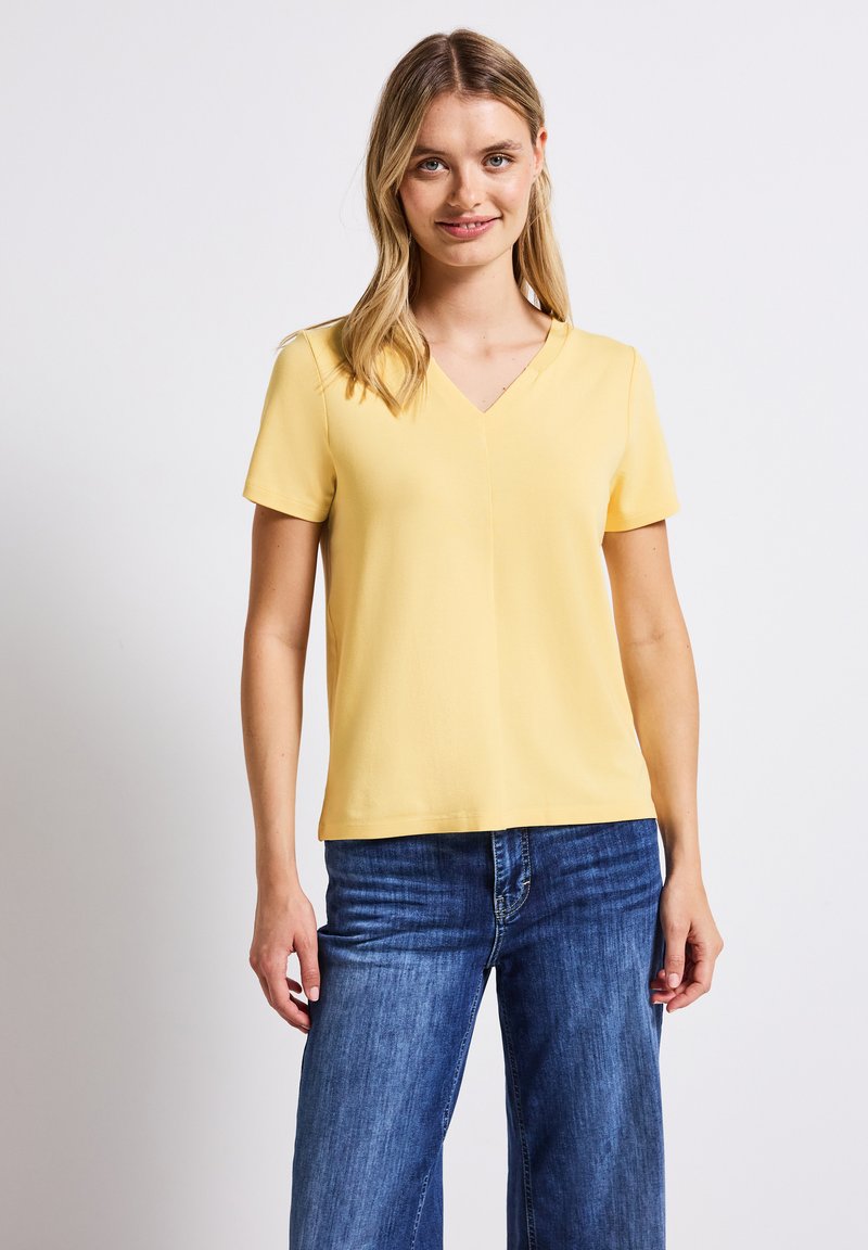 Geel V-hals T-shirt met korte mouwen, gemaakt van gladde stof, gecombineerd met blauwe denim wijde jeans. Eenvoudig ontwerp, zonder zichtbare patronen.