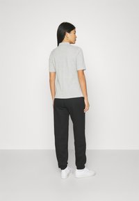 Graues Polo-Shirt mit kurzen Ärmeln, kombiniert mit schwarzen Jogginghosen. Das Outfit zeichnet sich durch eine lockere Passform und ein minimalistisches Design aus. Weiße Sneakers runden den Look ab.