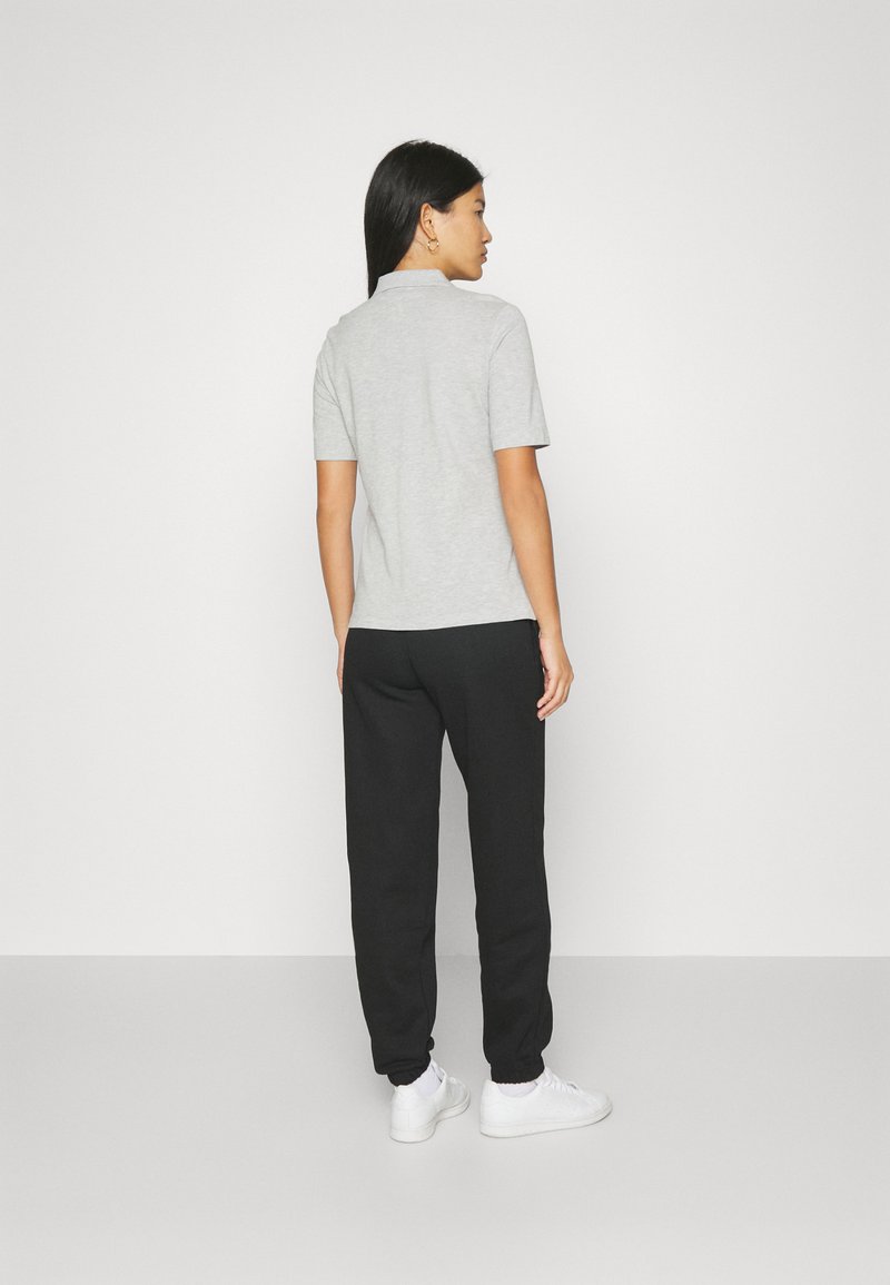 Szara koszulka polo z krótkim rękawem w zestawie z czarnymi spodniami dresowymi. Strój charakteryzuje się luźnym krojem i minimalistycznym stylem. Białe sneakersy dopełniają całość.