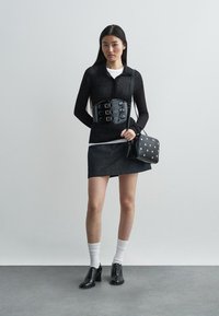 Čierny top s dlhým rukávom, rifľová sukňa, čierny korzetový opasok, čierna kabelka s bielymi bodkami, biele ponožky, čierne topánky. Minimalistický, moderný dizajn.