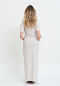 Abito a maglia attillato di colore beige chiaro con maniche corte e silhouette lunga e dritta, abbinato a scarpe marroni scure. Tessuto liscio, design minimale.