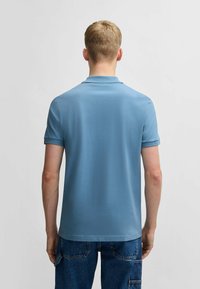 Ljusblå polo med korta ärmar och ribbat krage, tillverkad av mjukt tyg, bärs med denimshorts. Inga synliga mönster eller accenter.