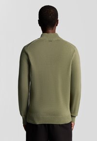 Pull en tricot vert avec un col montant, des poignets et un ourlet à côtes, et une finition texturée, vu de dos.