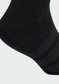 Calcetín de algodón negro con textura acanalada, diseño sin costuras y talón reforzado para mayor durabilidad. Acabado suave con un patrón sutil en la parte superior.