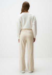 Pantalons beiges à jambes larges avec une taille élastique, accompagnés d'un sweatshirt blanc avec des épaules tombantes et des poignets côtelés.