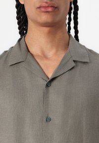 Camicia a maniche corte grigio chiaro con colletto a punta, texture sottile e due bottoni sul davanti, che offre una vestibilità comoda.