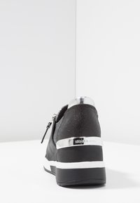 Sneaker nera con upper testurizzato, accentuazioni metalliche e tacco lucido. Presenta una chiusura con zip e una suola bianca con bordo nero.