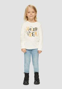 Langärmliges cremefarbenes Hemd mit schwarzem und orangefarbenem "HALLOWEEN"-Grafik, kombiniert mit hellblauen Skinny-Jeans und schwarzen Schnürstiefeln.