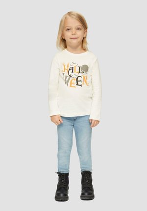 Biała koszula z długim rękawem z grafiką "HALLOWEEN" w czarnym i pomarańczowym kolorze, w zestawieniu z jasnoniebieskimi skinny jeansami i czarnymi butami na sznurówki.