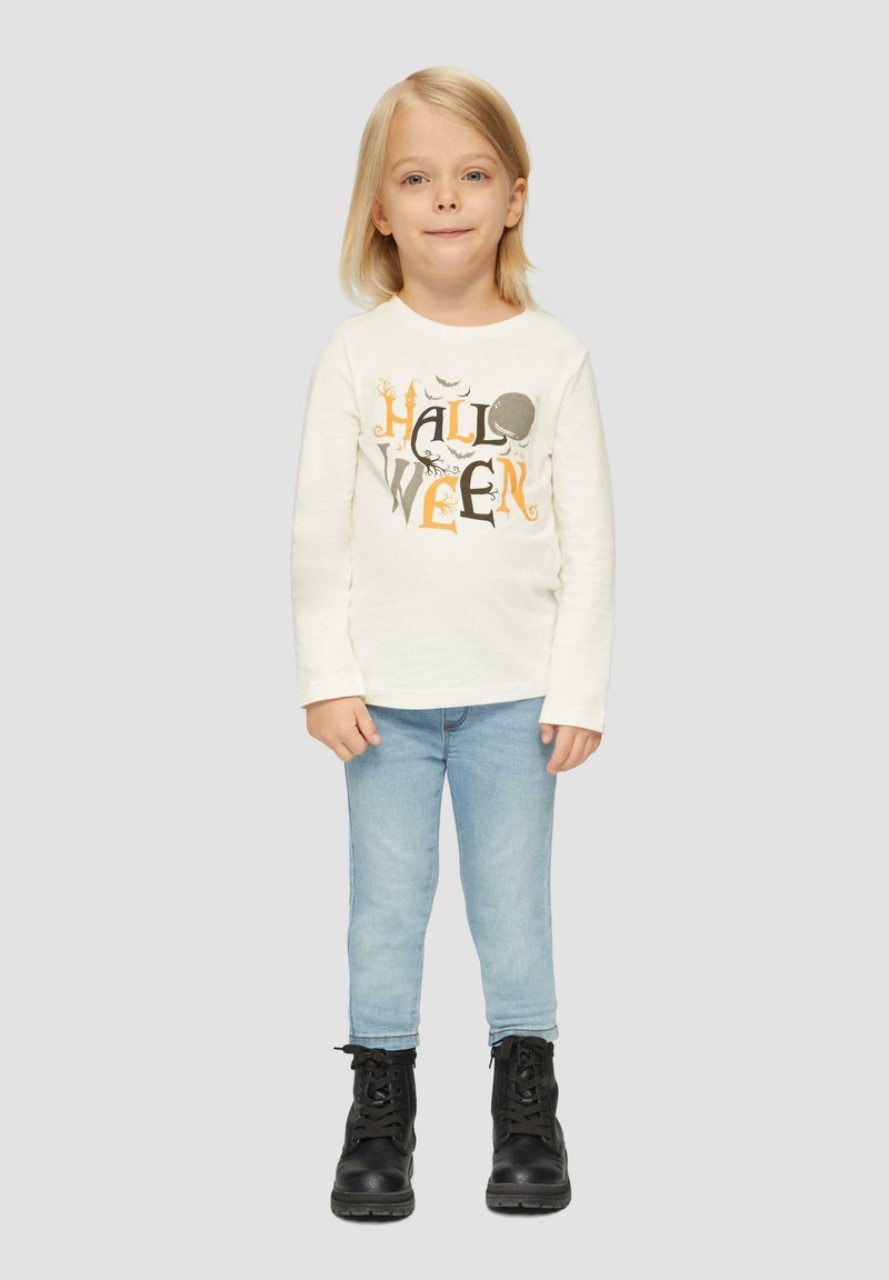 Langärmliges cremefarbenes Hemd mit schwarzem und orangefarbenem "HALLOWEEN"-Grafik, kombiniert mit hellblauen Skinny-Jeans und schwarzen Schnürstiefeln.