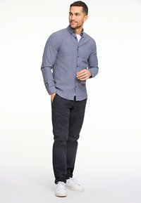 Langarm, knoopsluiting overhemd in het blauw, gecombineerd met donkere broek en witte sneakers. Heeft een puntige kraag en een detail van een voorzak.